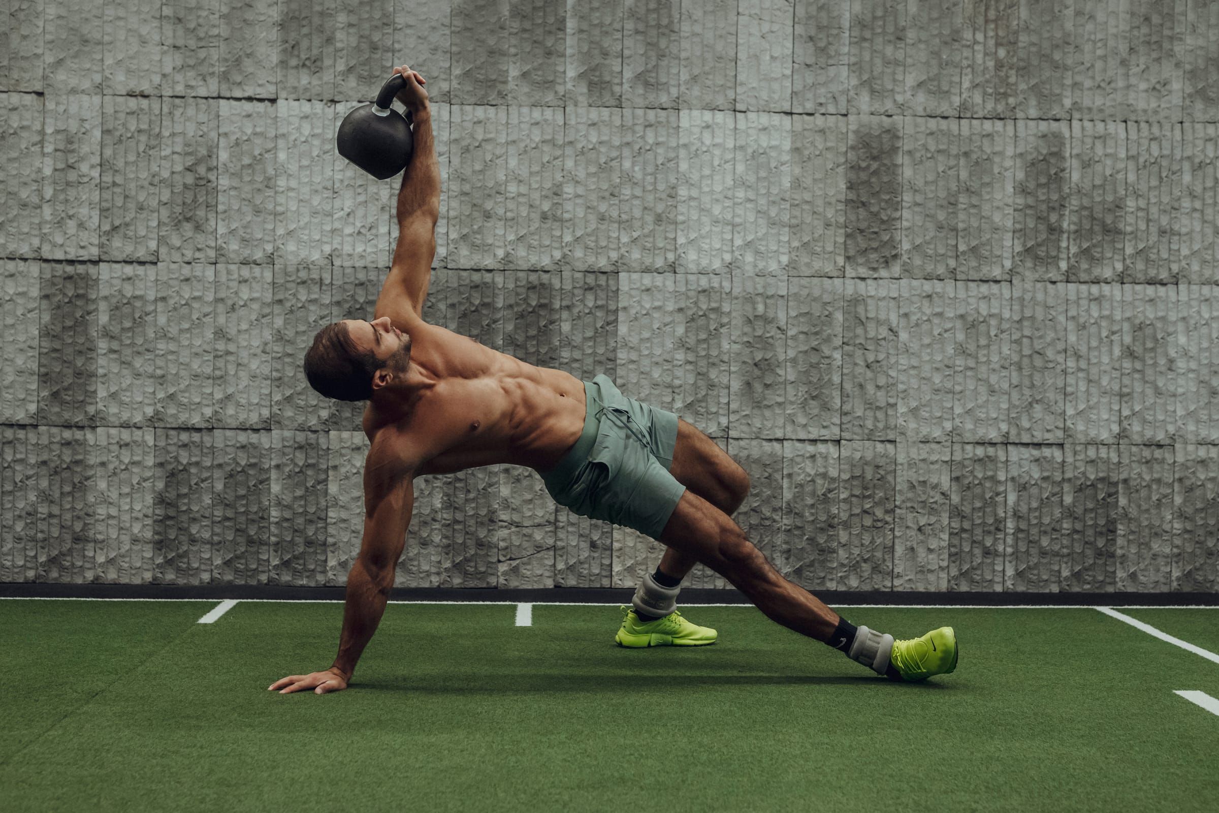 Sultan holding a side plank with a kettlebell pressed overhead